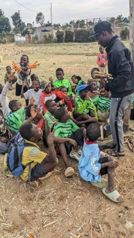 Boys sitting on the grass looking up at a coach holding sugarcane