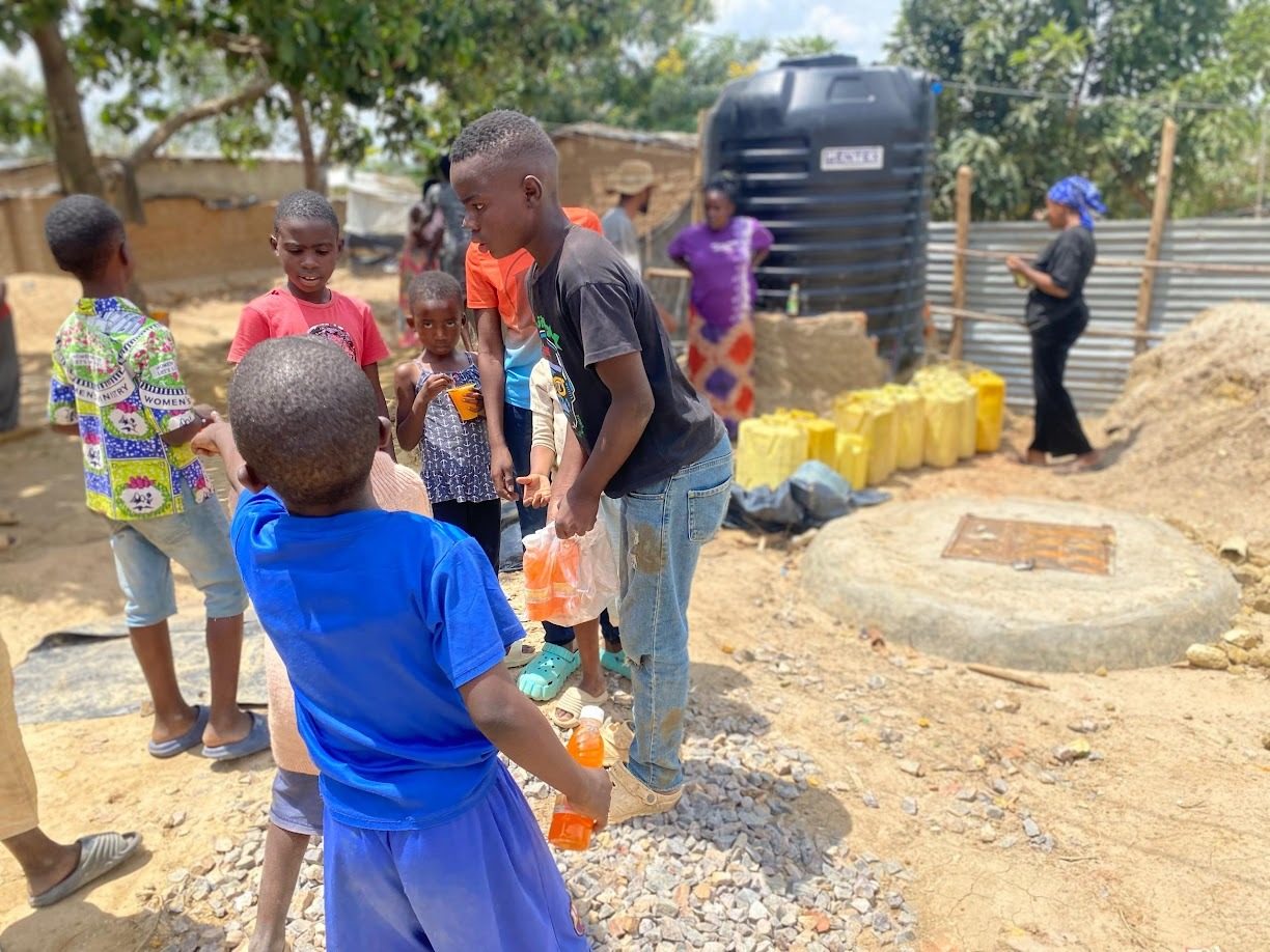 Children laughing as they fill jerrycans at a community water tank in Nakivale
