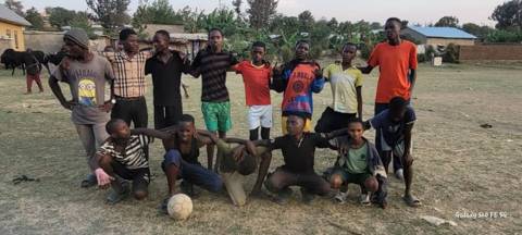 Older and younger players posing together on the pitch with a football, at dusk