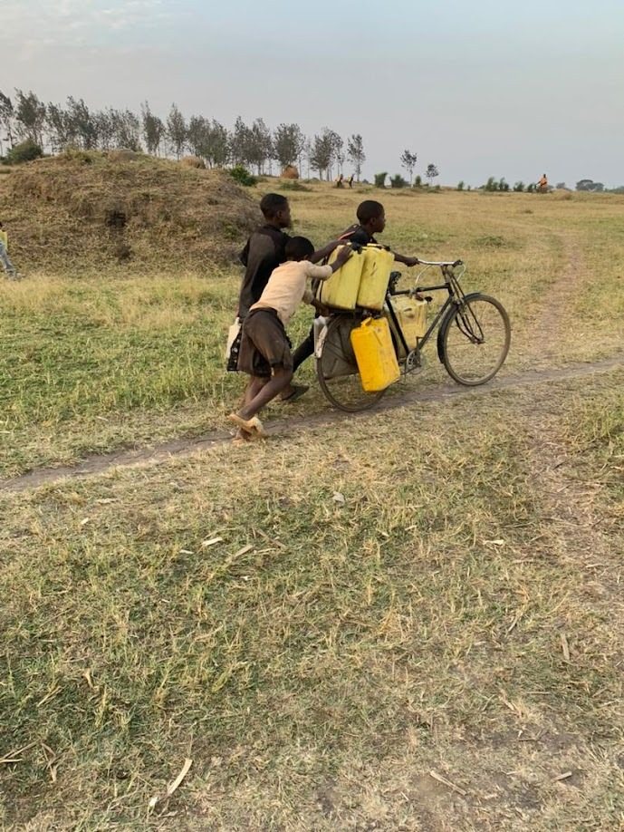 Children pushing a bicycle loaded with jerrycans along a settlement road