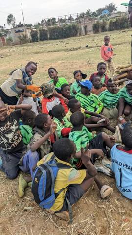 Boys in green shirts sitting close together on the grass, smiling at the camera