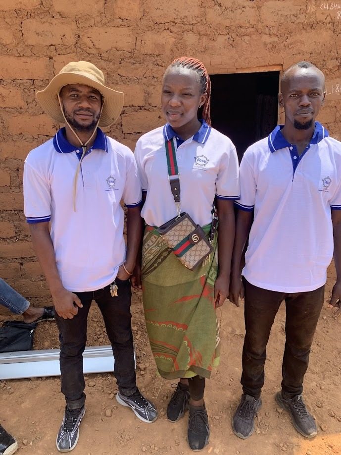 Three YRUD members in branded shirts standing together in the settlement