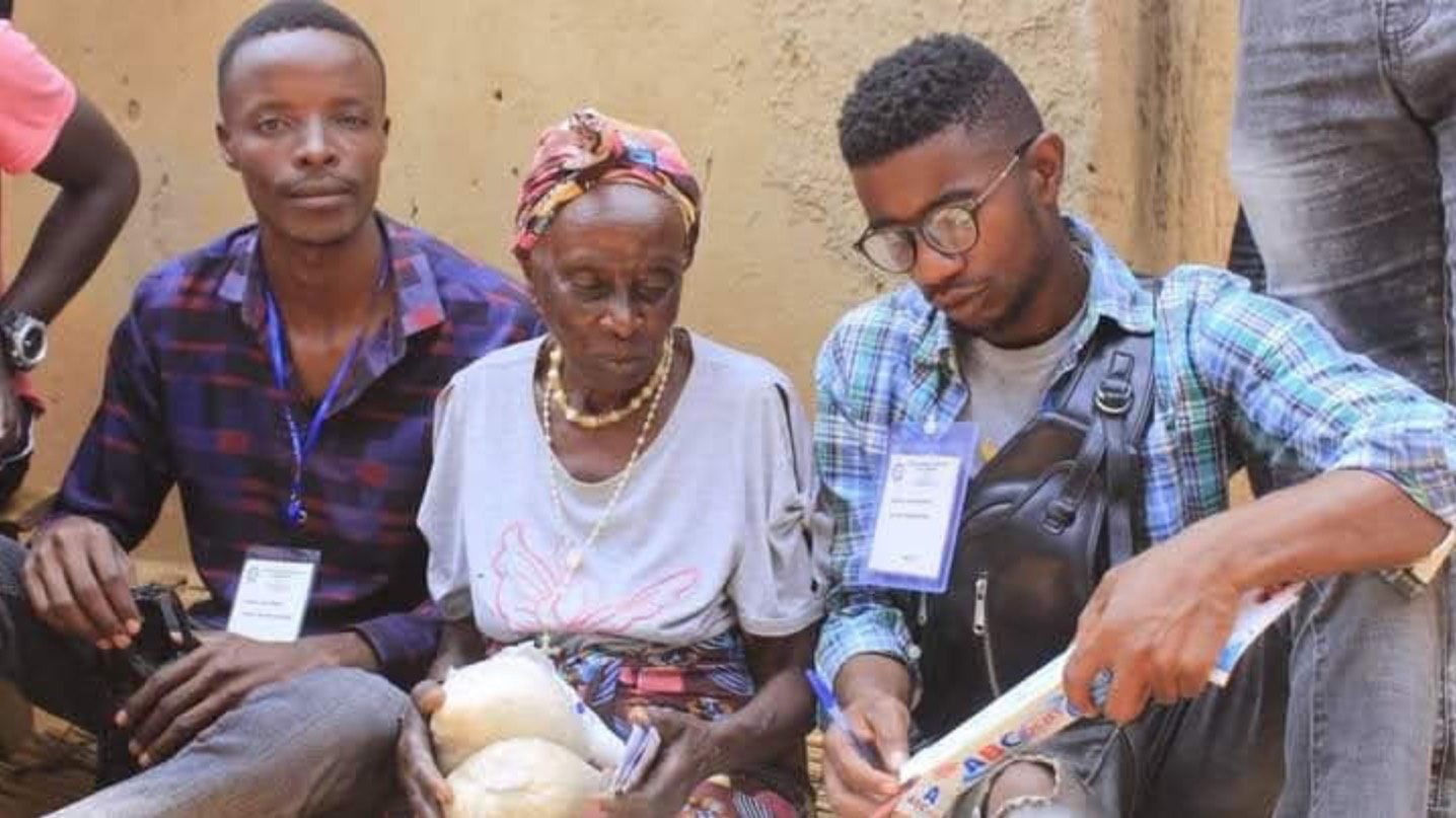 Two YRUD team members sitting with an elder during a community outreach in Nakivale, registering her and handing over supplies.
