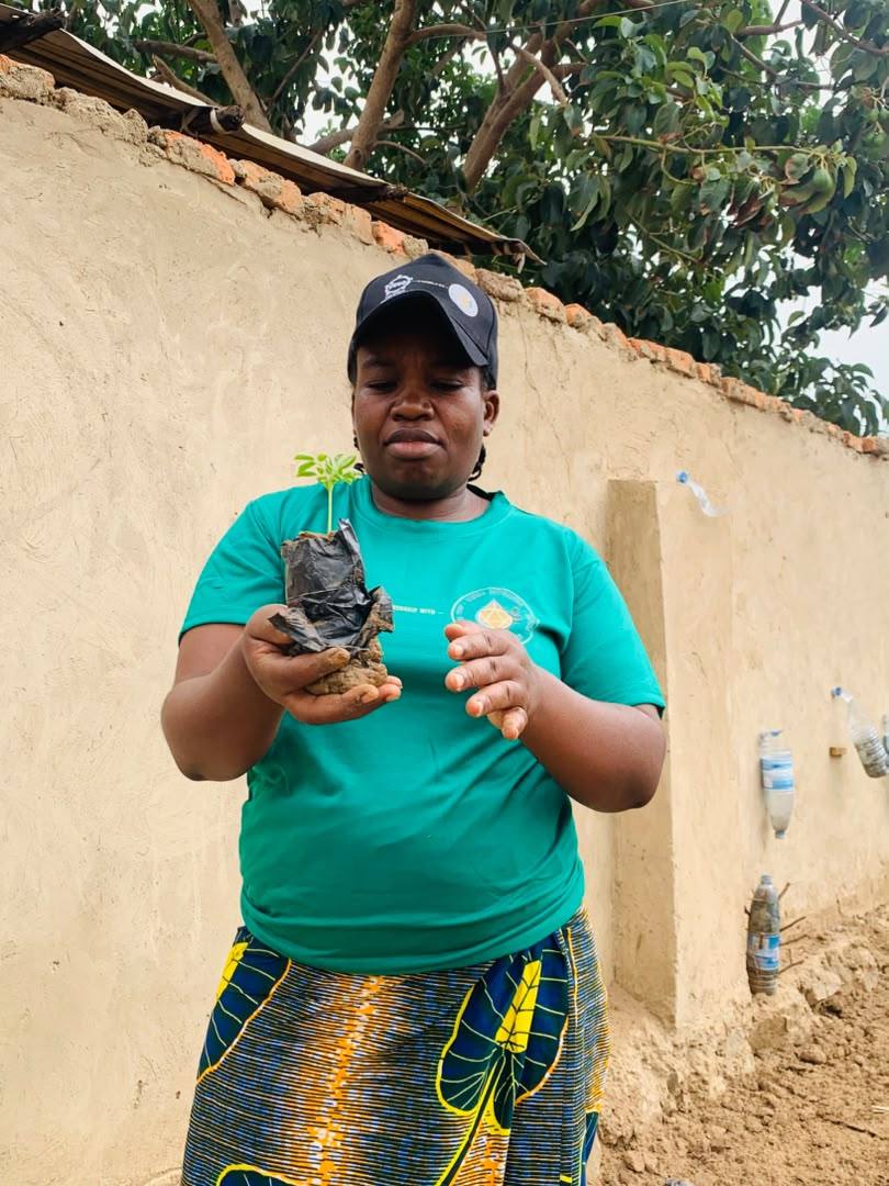 A YRUD member in a green team shirt holding a young moringa seedling in its planting bag